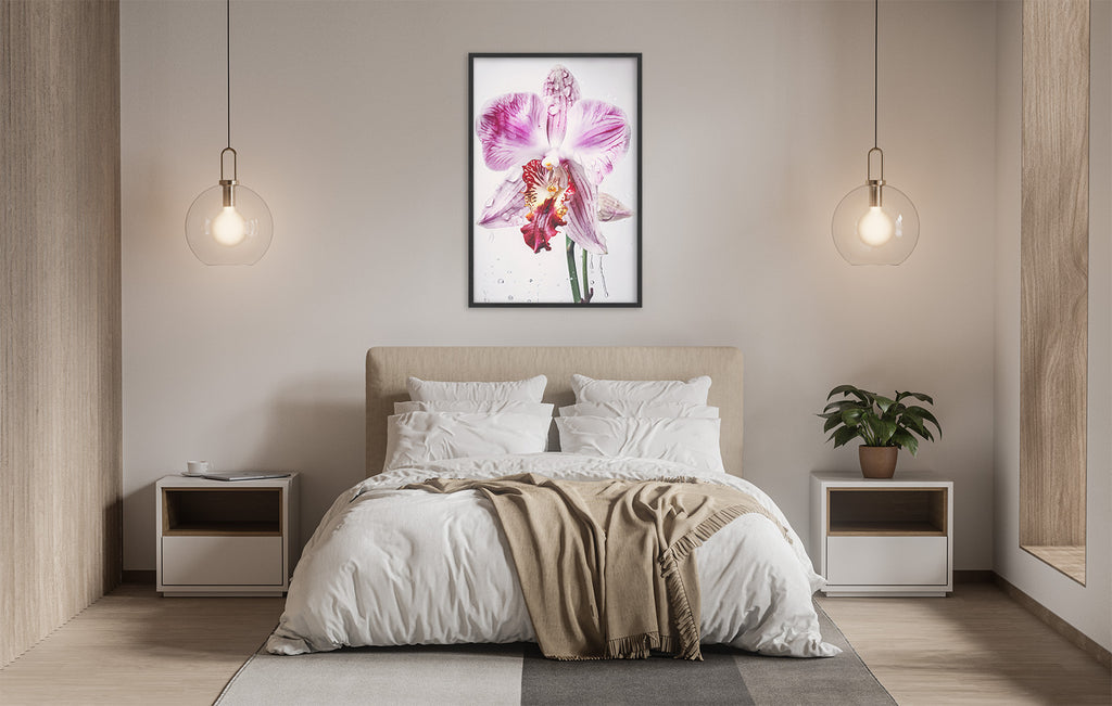 a serene and modern bedroom with a large bed, white bedding, and a framed picture of a pink orchid flower hanging above it. The room is illuminated by two pendant lights, creating a warm and inviting atmosphere.