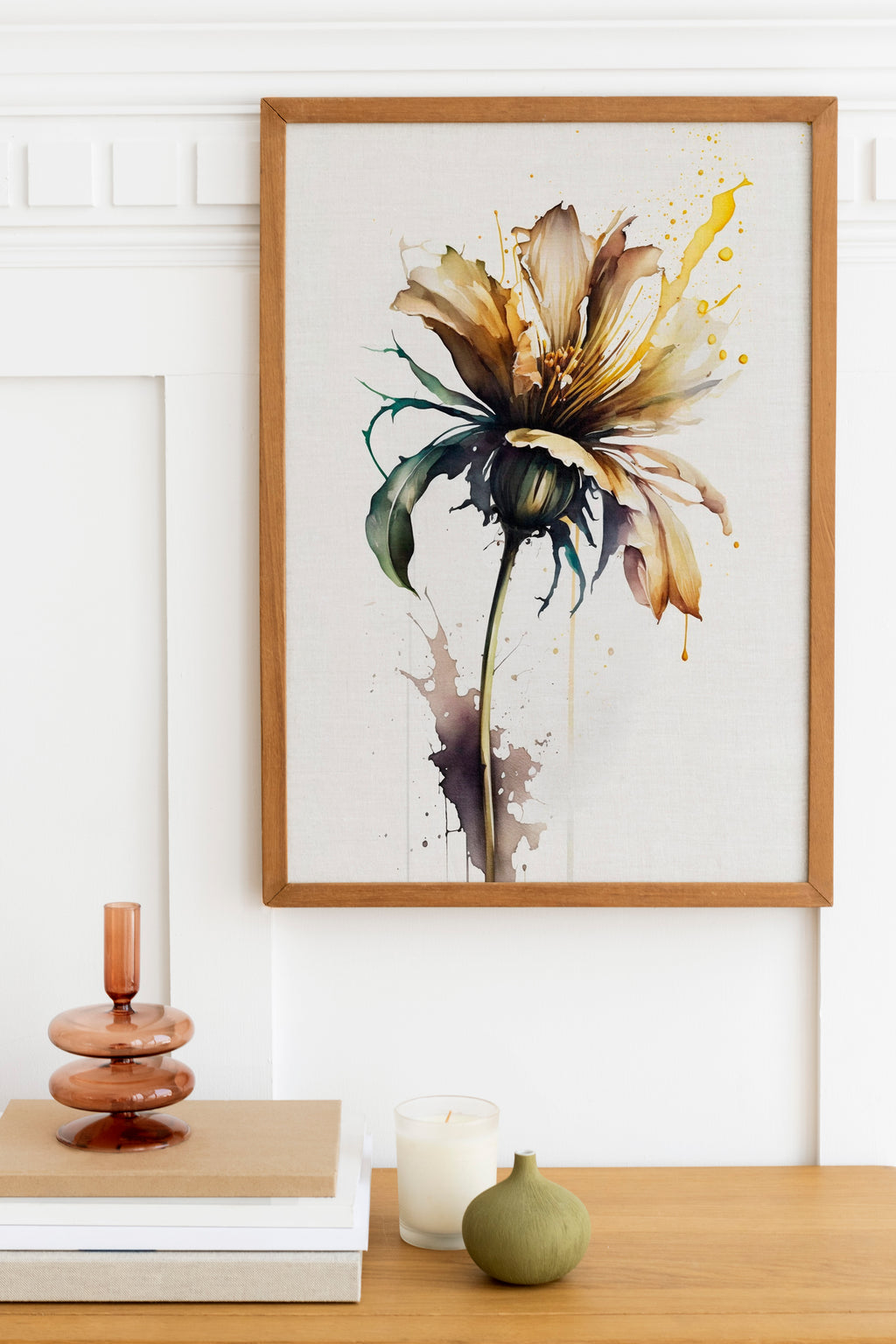 a framed painting of a yellow flower with green leaves, hanging on a white wall above a wooden table with various decorative items on it.