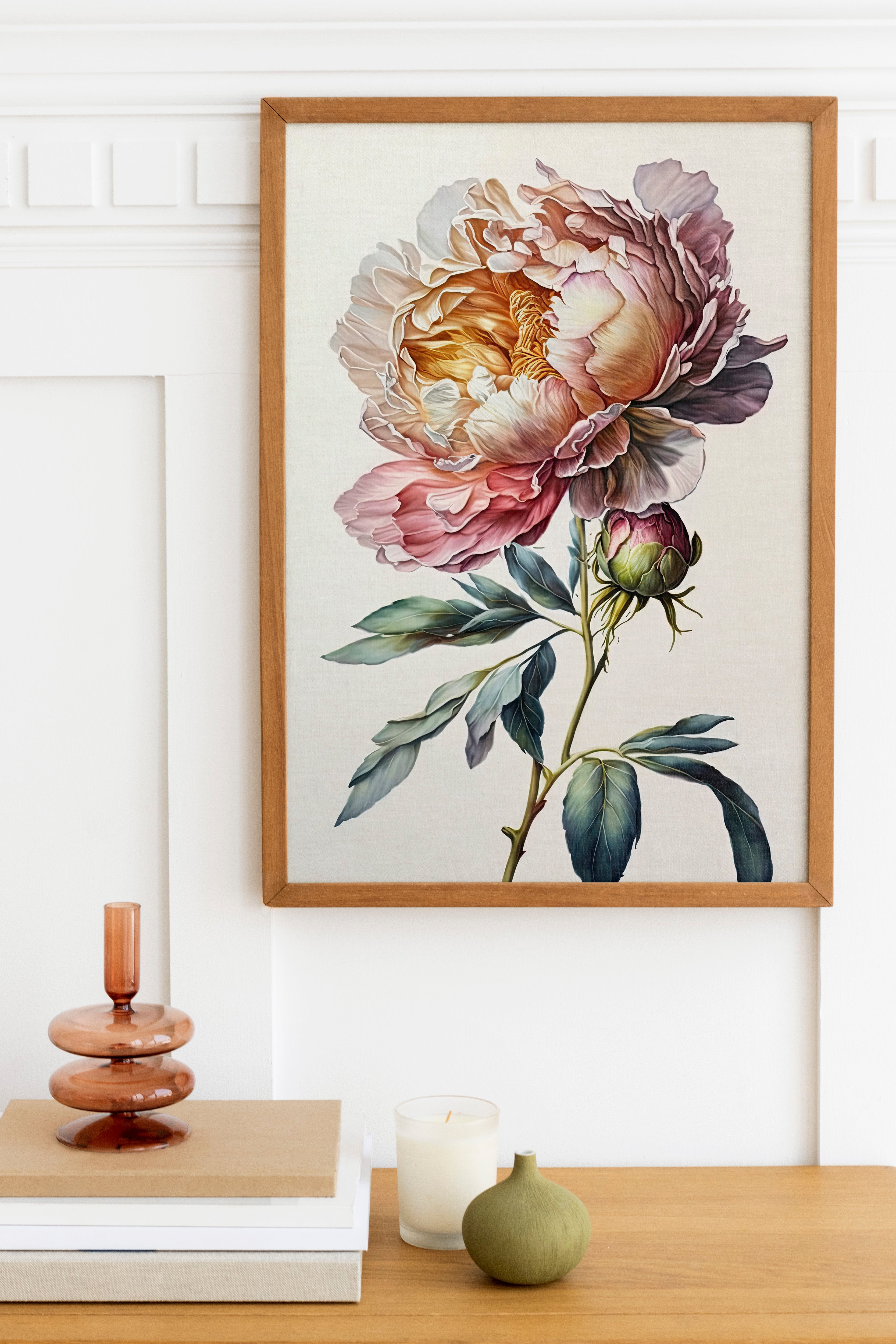 a framed painting of a large, colorful flower hanging on a wall above a wooden table with various decorative items, including a candle, a small green vase, and a stack of books.