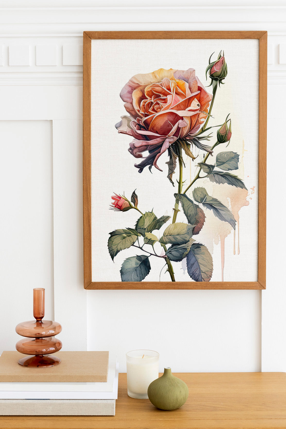 a framed painting of a large, vibrant rose on a white wall, with a wooden shelf below it holding a stack of books, a small green vase, and a white candle.