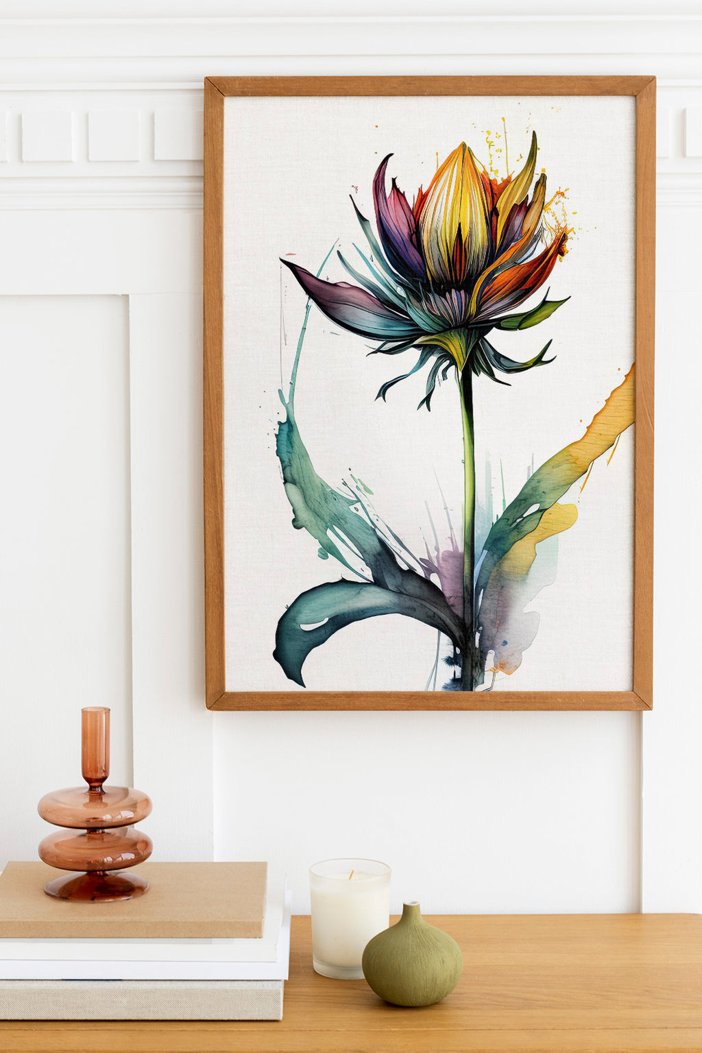 a framed painting of a colorful flower hanging on a wall above a wooden table with various decorative items, including a candle, a stack of books, and a small green vase.
