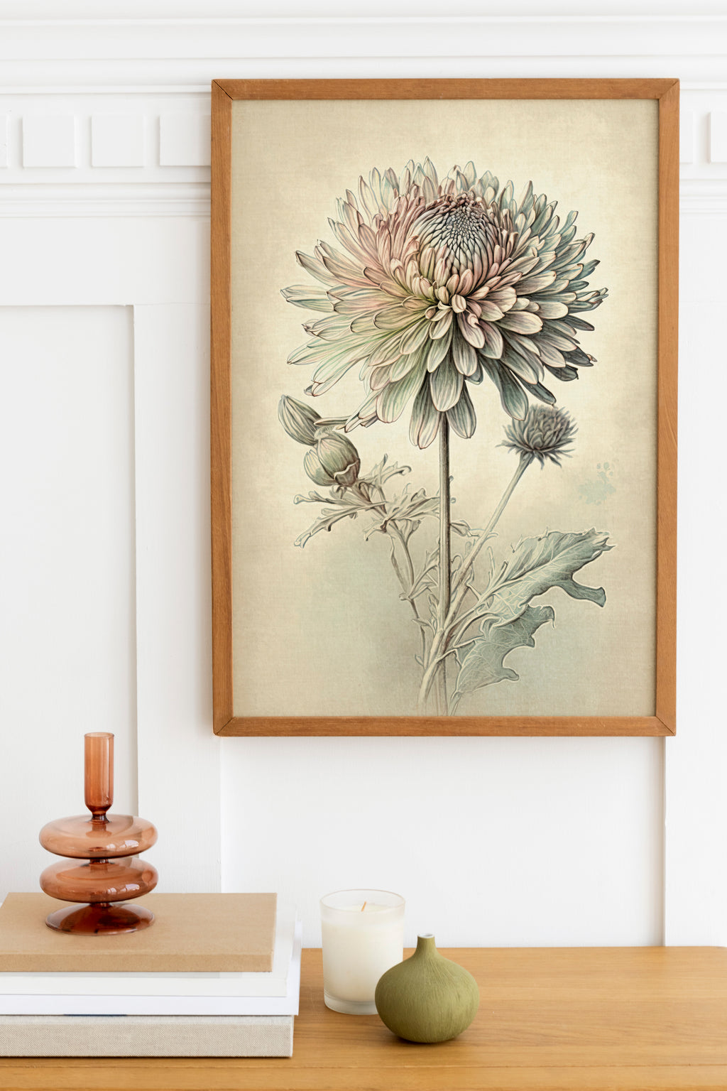 a framed botanical illustration of a flower, which is hanging on a wall above a wooden table. On the table, there is a stack of books, a small green vase, and a white candle.