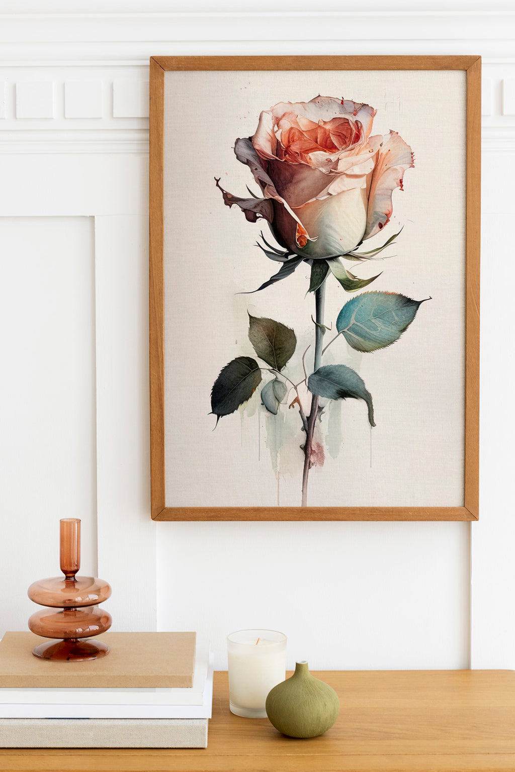 a framed painting of a pink rose hanging on a wall, with a wooden shelf below it holding a stack of books, a small green vase, and a white candle.