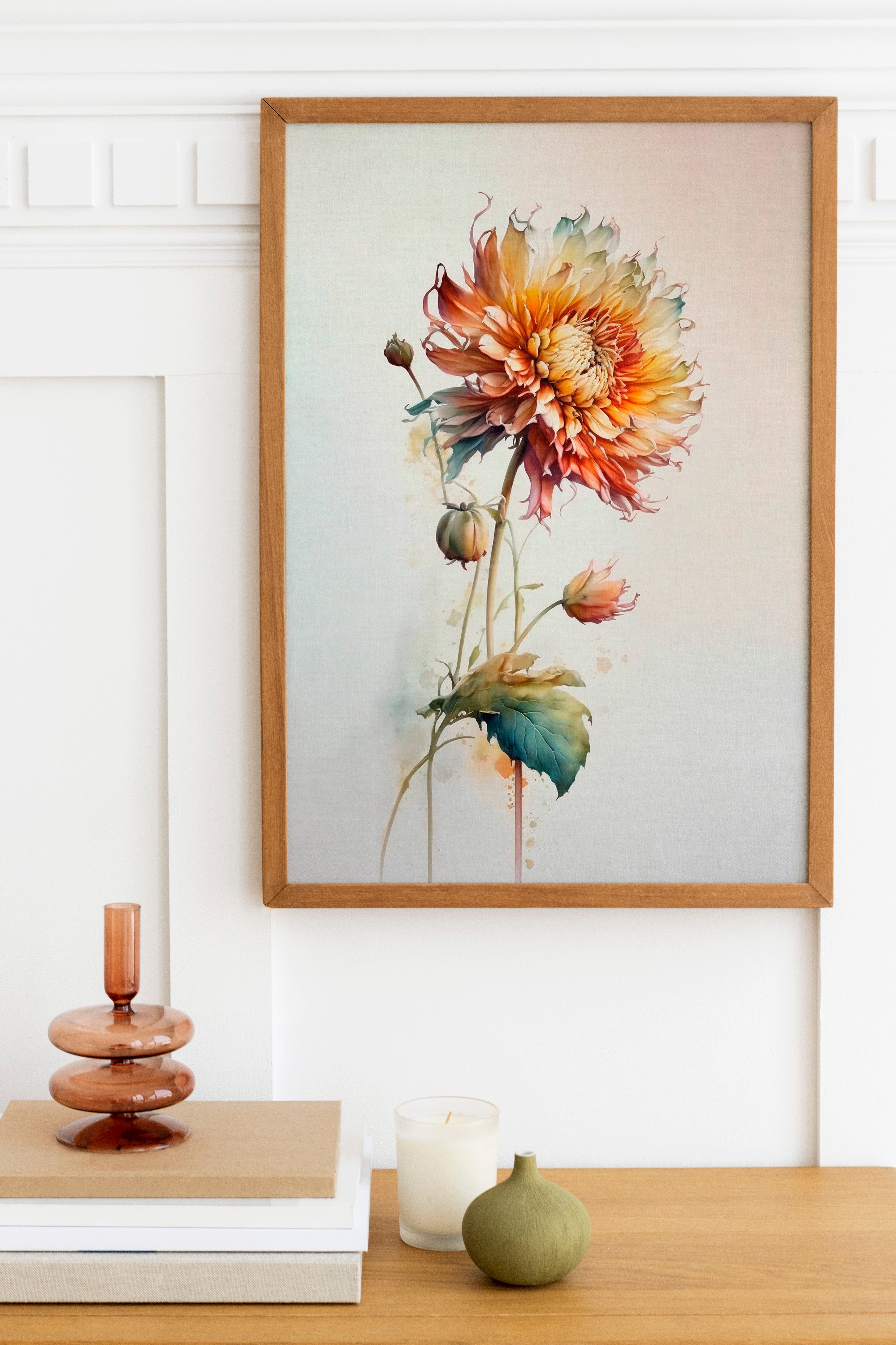 a wooden table with a framed painting of a vibrant flower hanging above it. The table also has a stack of books, a small green vase, and a white candle.