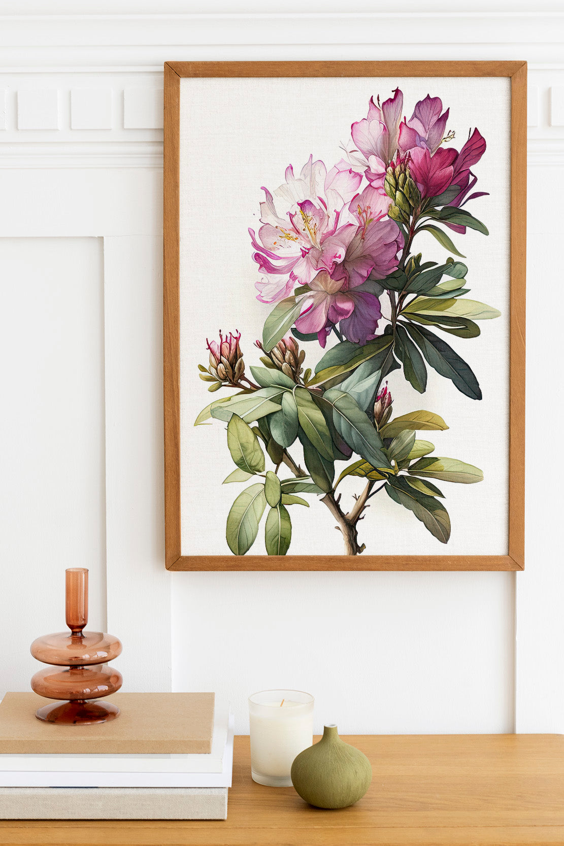 a framed painting of a flower on a wall, with a wooden shelf below it holding a stack of books, a small green vase, and a white candle.
