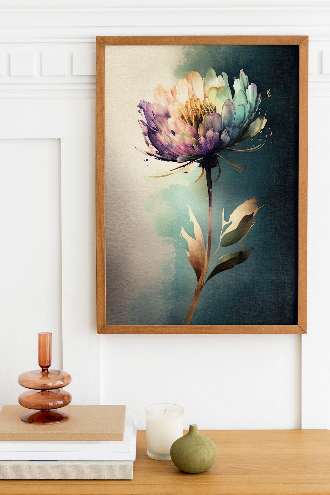 a framed painting of a colorful flower hanging on a wall above a wooden table with various decorative items, including a candle, a small green vase, and a stack of books.