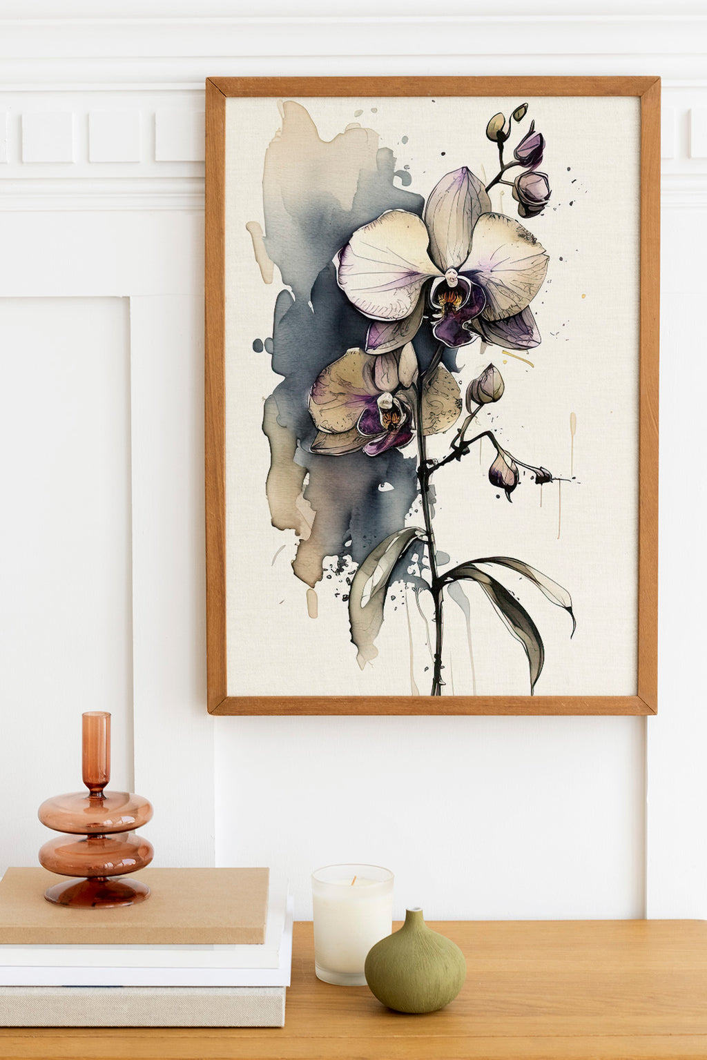 a framed painting of a purple orchid flower hanging on a wall above a wooden table with various decorative items, including a candle, a small green vase, and a stack of books.
