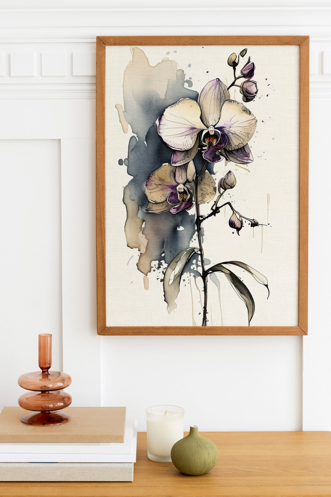 a framed painting of a purple orchid flower hanging on a wall above a wooden table with various decorative items, including a candle, a small green vase, and a stack of books.