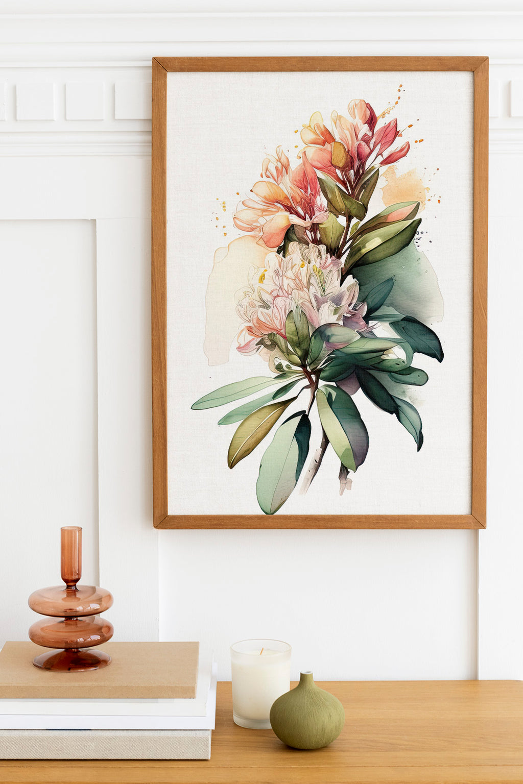 a framed watercolor painting of a vibrant floral arrangement hanging on a white wall above a wooden table. The table also holds a stack of books, a small green vase, and a white candle.
