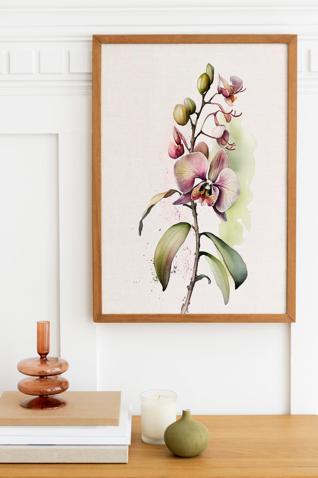a framed painting of a purple orchid plant hanging on a wall above a wooden table with various decorative items, including a stack of books, a candle, and a small green vase.