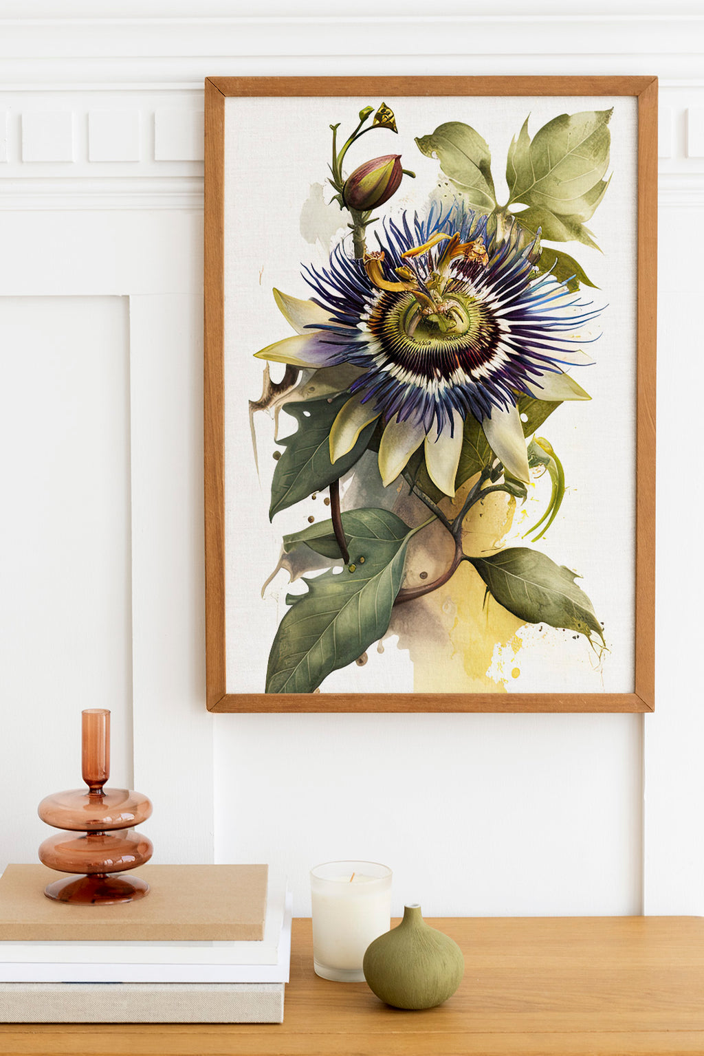 a framed painting of a vibrant blue and purple flower with green leaves, hanging on a white wall above a wooden table. On the table, there is a stack of books, a small green vase, and a white candle.