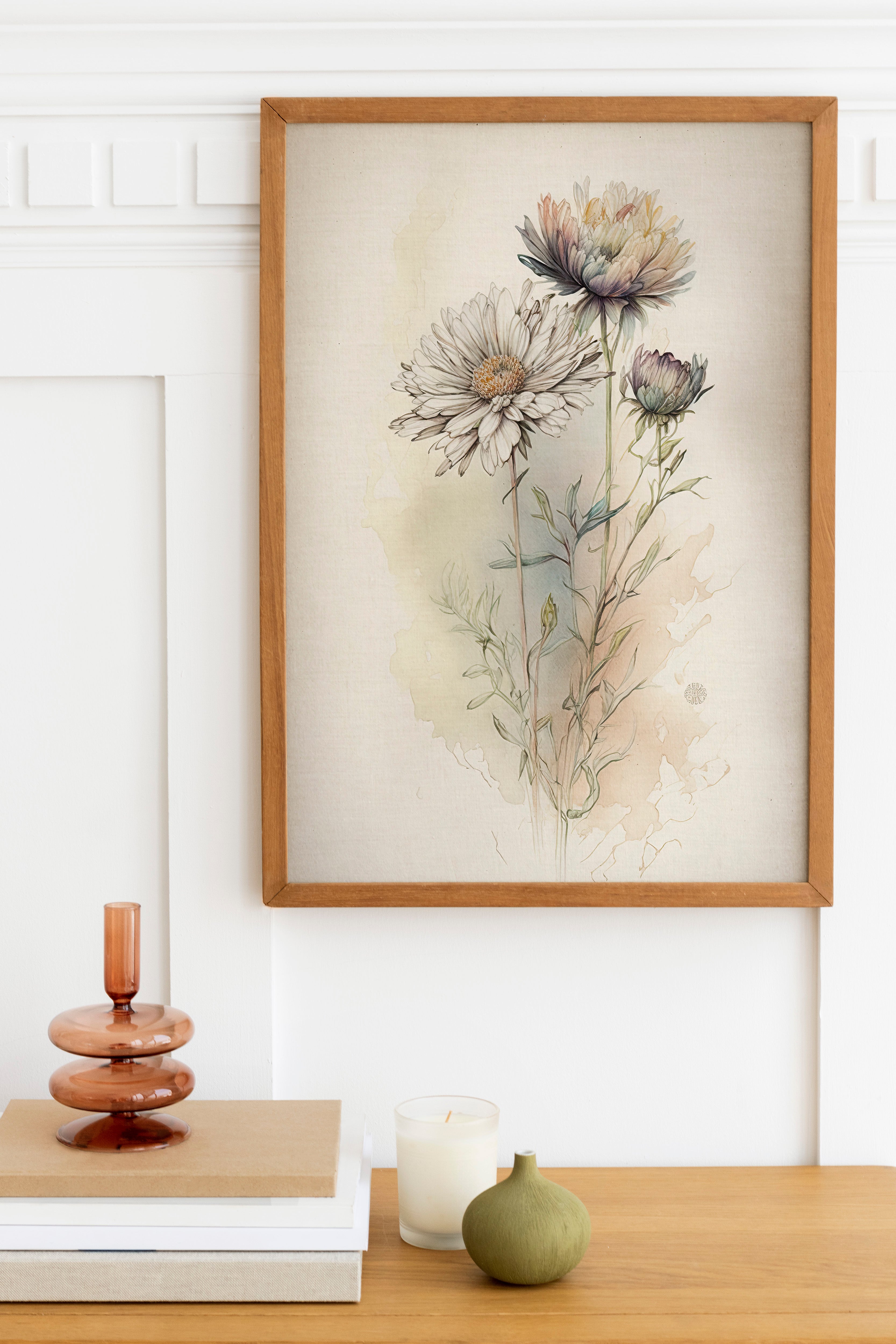 a framed painting of flowers hanging on a wall above a wooden table with various decorative items on it, including a stack of books, a small green vase, and a white candle.