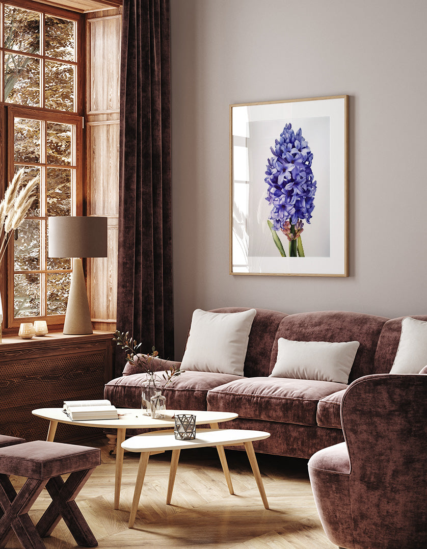 a cozy living room with a large window, a brown sofa, a wooden coffee table, and a framed picture of a purple flower on the wall.