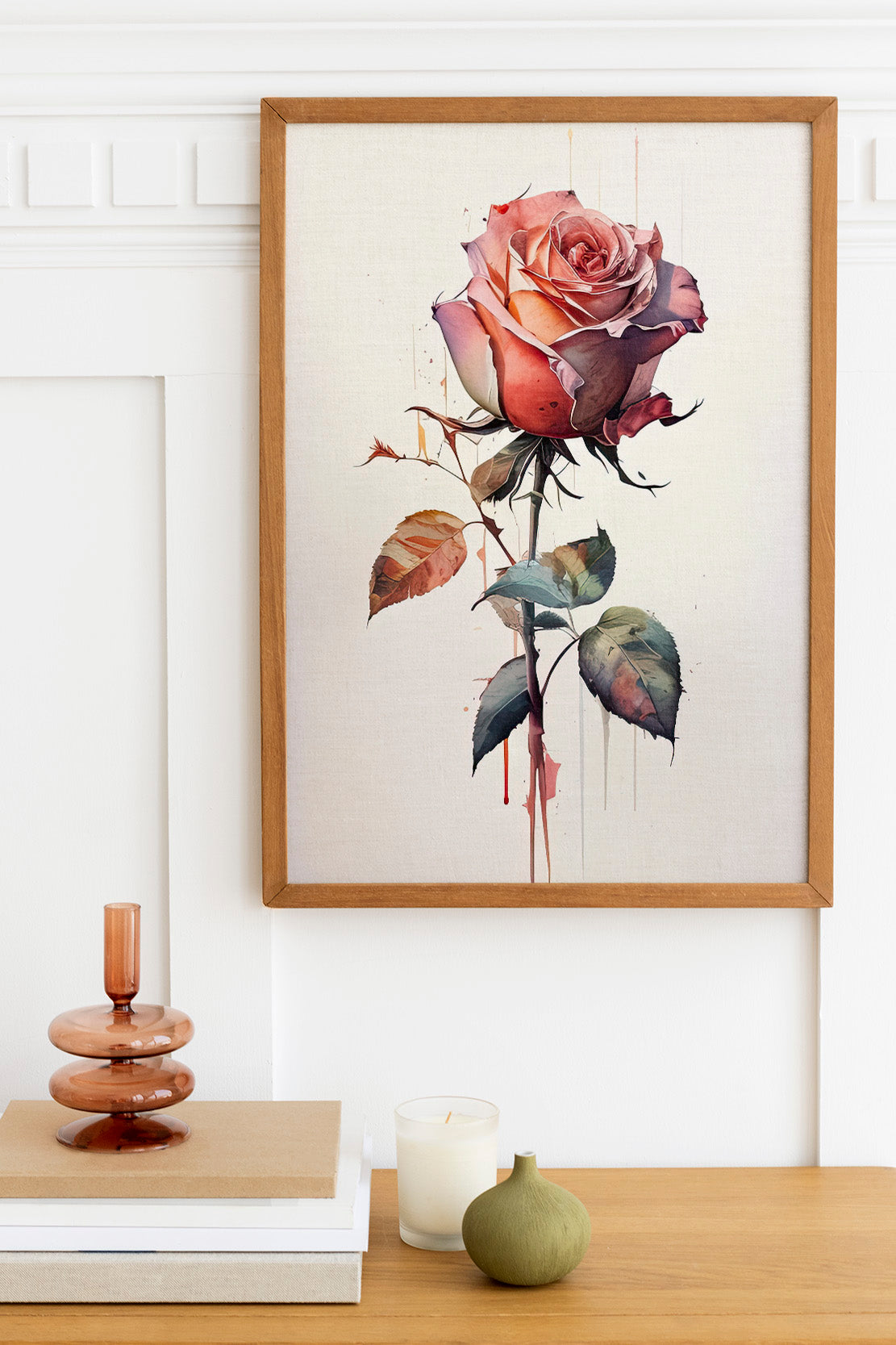 a framed painting of a pink rose hanging on a wall, with a wooden shelf below it holding a stack of books, a small green vase, and a white candle.