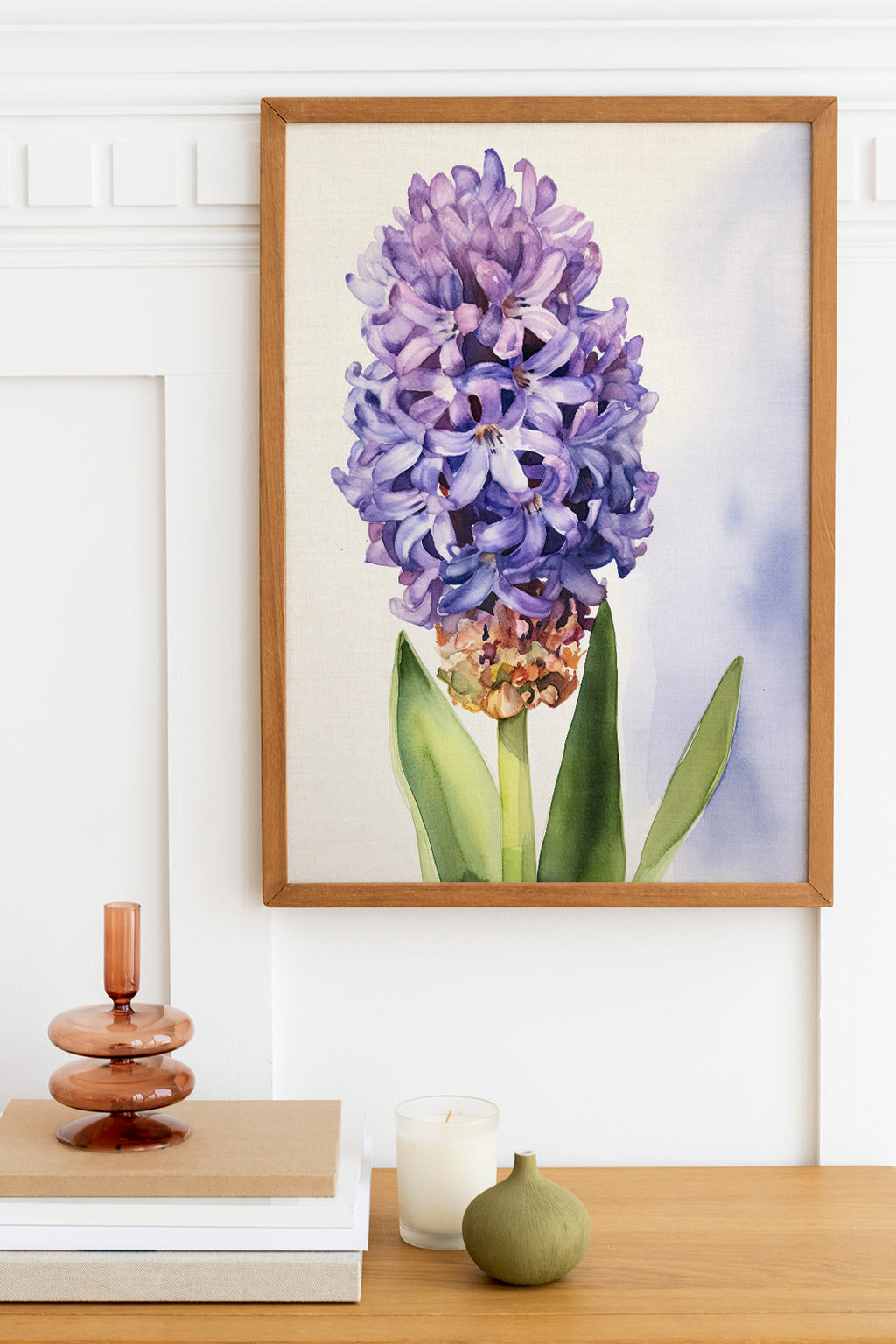 a framed painting of a purple hyacinth flower hanging on a wall above a wooden table with various decorative items on it.