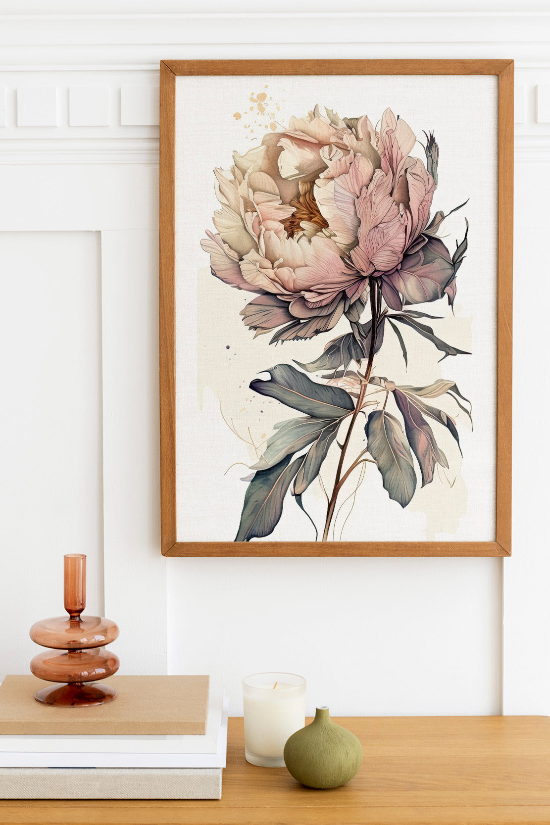 a framed painting of a large, detailed peony flower hanging on a wall above a wooden table. The table has a stack of books, a small green vase, and a white candle.