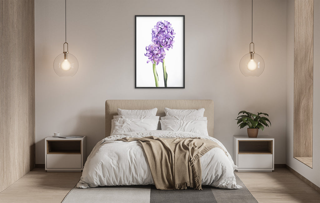 a serene and modern bedroom with a large bed, white bedding, and a framed picture of purple flowers hanging above it. The room is illuminated by two pendant lights, creating a warm and inviting atmosphere.
