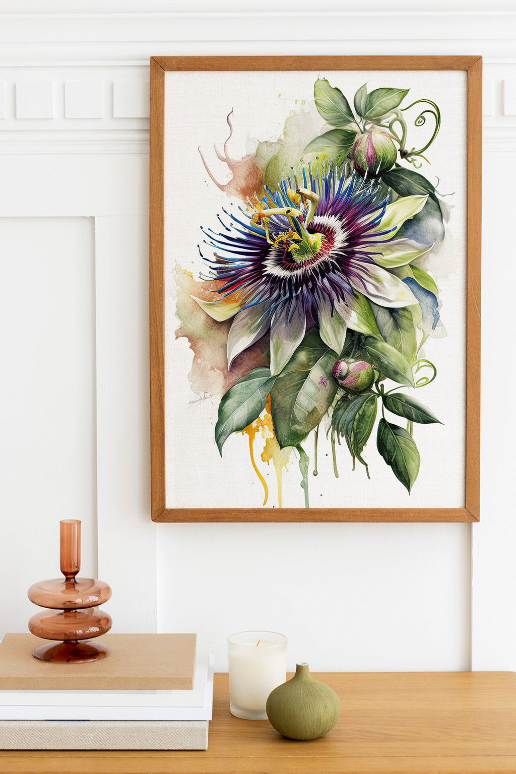 a framed painting of a vibrant, colorful flower with lush green leaves, hanging on a white wall above a wooden table. The table also holds a small vase, a stack of books, and a candle.