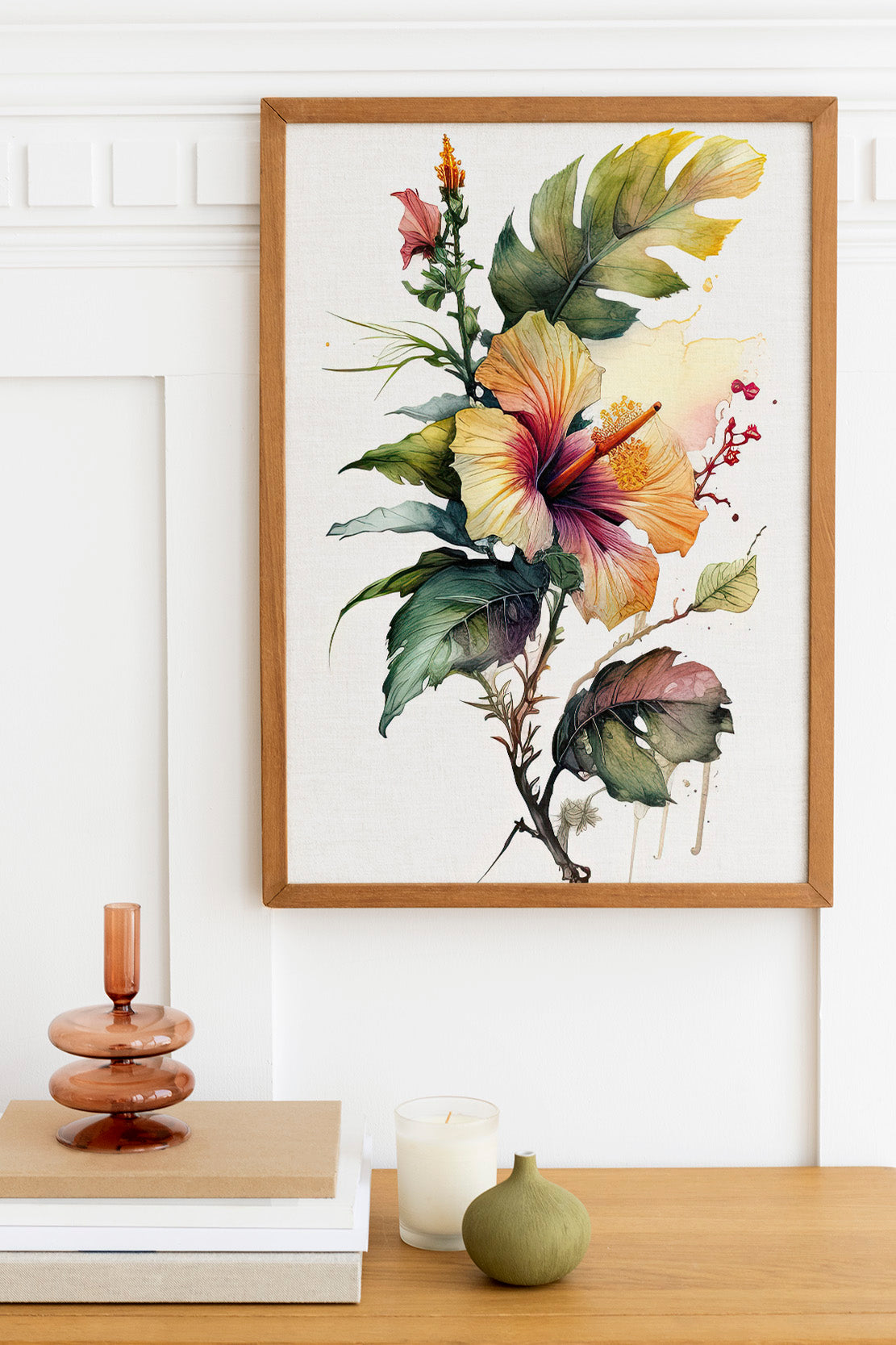 a framed painting of a vibrant hibiscus flower on a white wall, with a wooden shelf below it holding a stack of books, a small green vase, and a white candle.