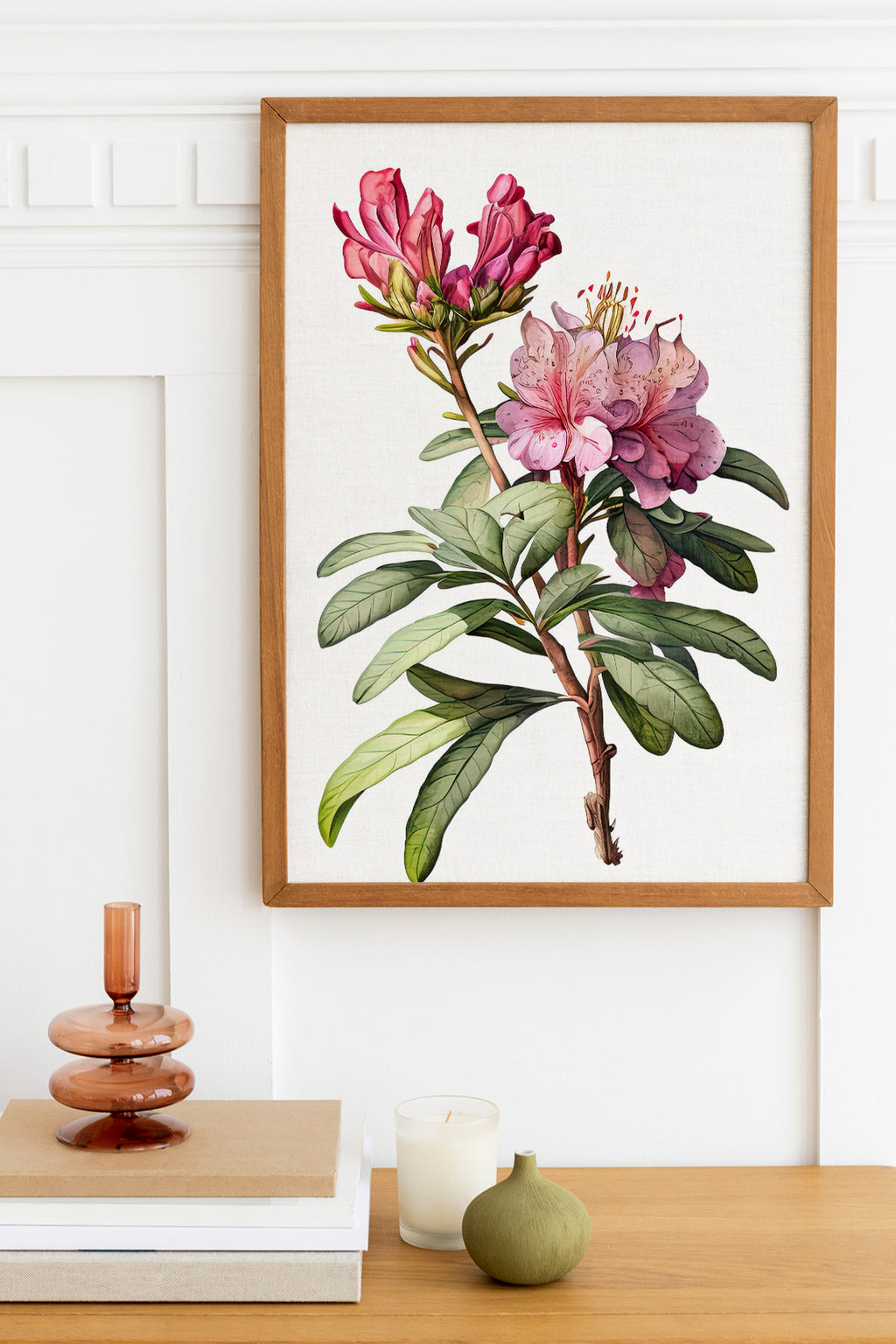 a framed botanical illustration of a pink flower on a white background, hanging on a wall above a wooden table with various decorative items on it.
