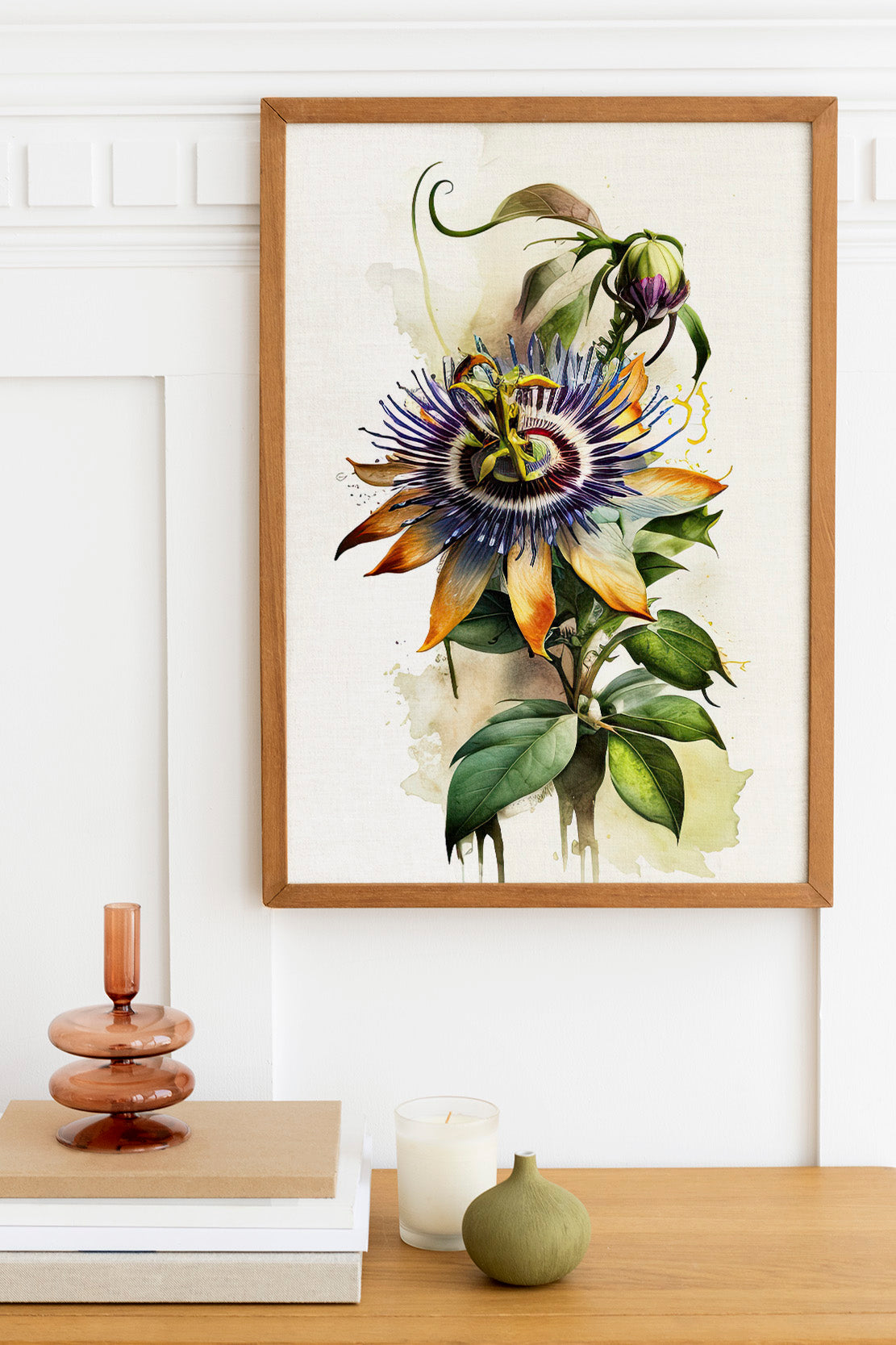 a framed painting of a vibrant, colorful flower hanging on a wall above a wooden table. The table also holds a stack of books, a small green vase, and a white candle.