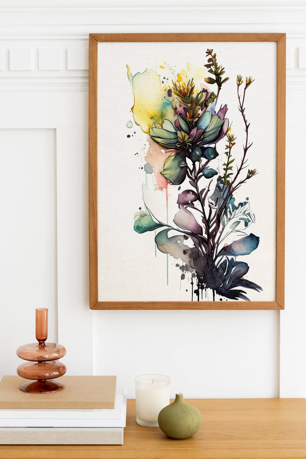 a framed watercolor painting of a vibrant floral arrangement hanging on a white wall above a wooden table. The table also holds a stack of books, a small green vase, and a white candle.