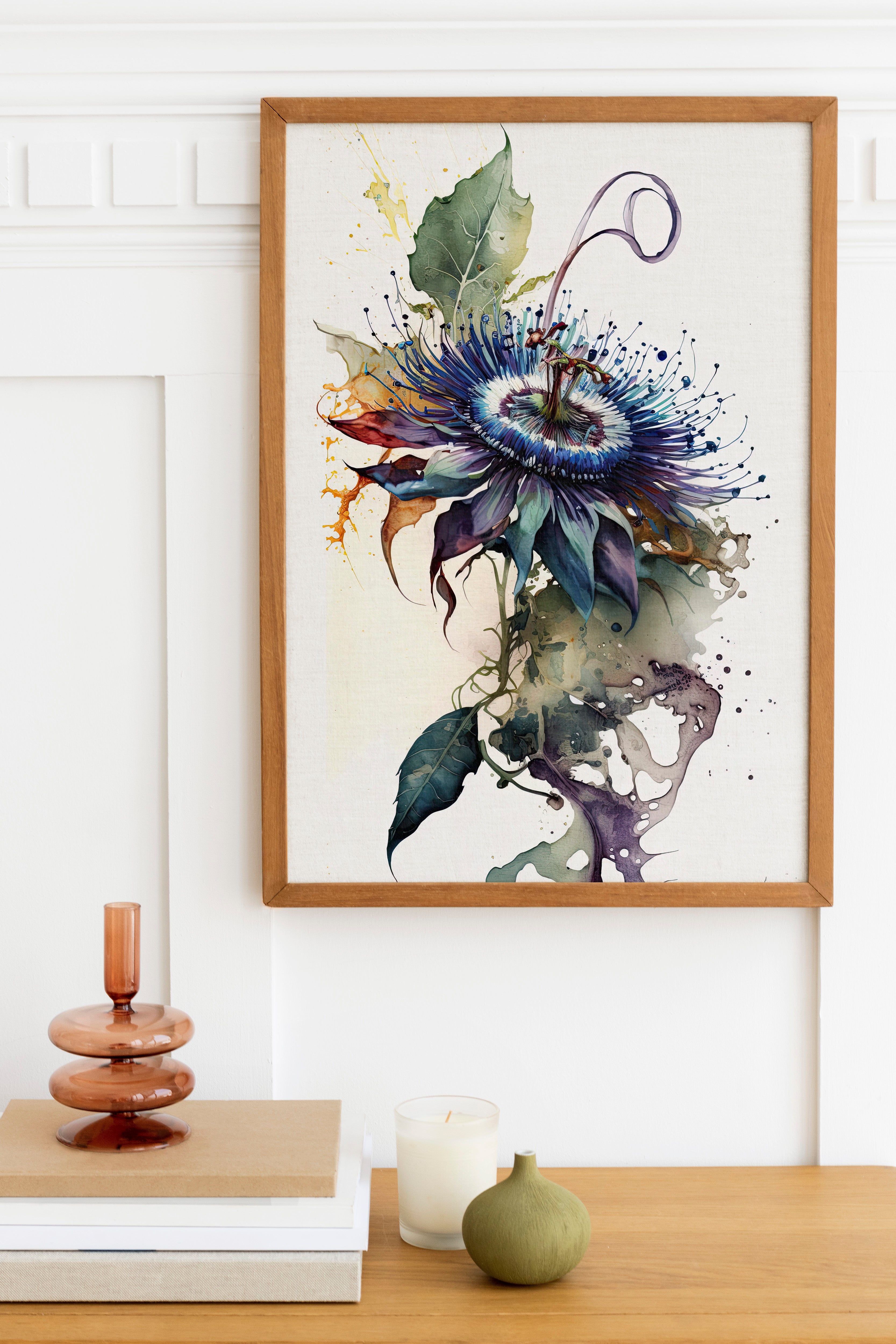 a framed painting of a vibrant purple flower with green leaves, hanging on a white wall above a wooden table. On the table, there is a stack of books, a small green vase, and a white candle.