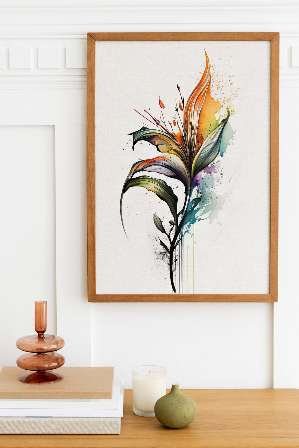 a framed painting of a colorful, abstract flower on a white wall above a wooden table with various decorative items, including a candle, a small green vase, and a stack of books.