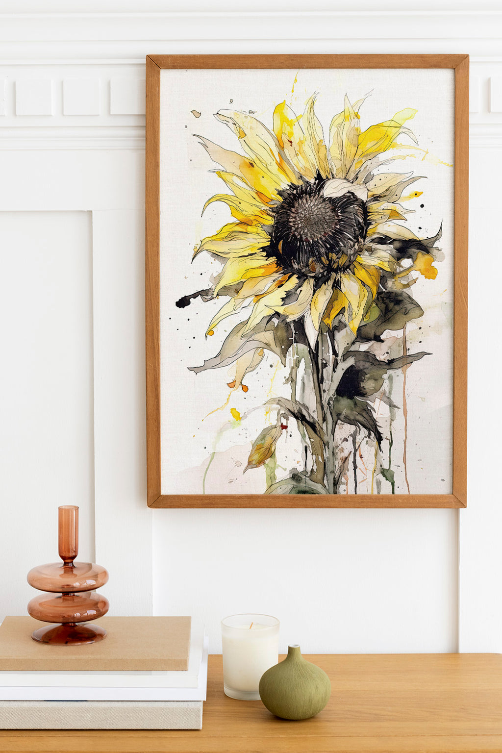 a framed watercolor painting of a yellow sunflower on a white background, hanging on a wall above a wooden table with various decorative items on it.