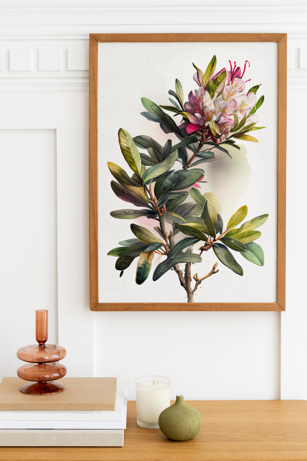 a framed botanical illustration of a plant with a pink flower, hanging on a white wall above a wooden table with various decorative items, including a candle, a small green vase, and a stack of books.