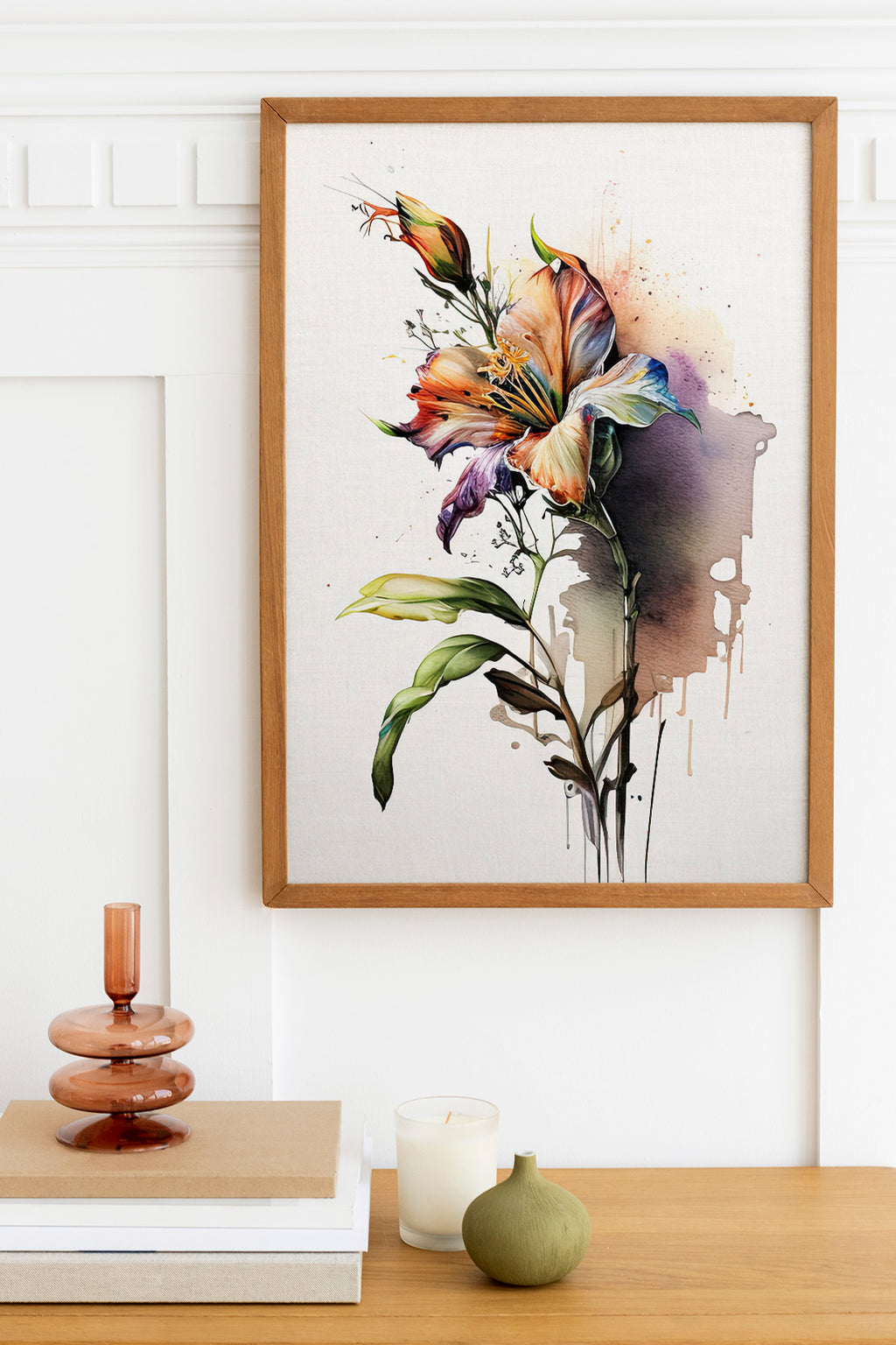 a framed painting of a colorful lily flower hanging on a wall above a wooden table with various decorative items, including a candle, a small green vase, and a stack of books.