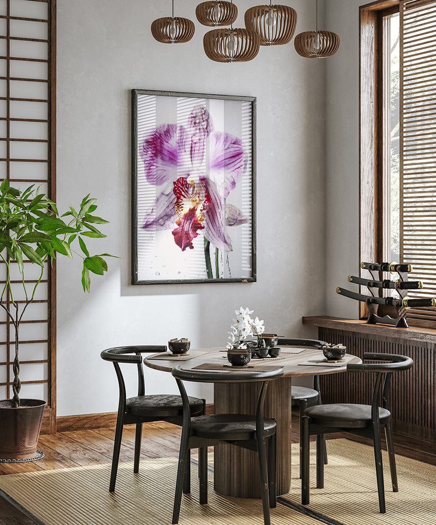 a modern dining room with a round wooden table, four black chairs, and a large framed orchid flower hanging on the wall above the table.