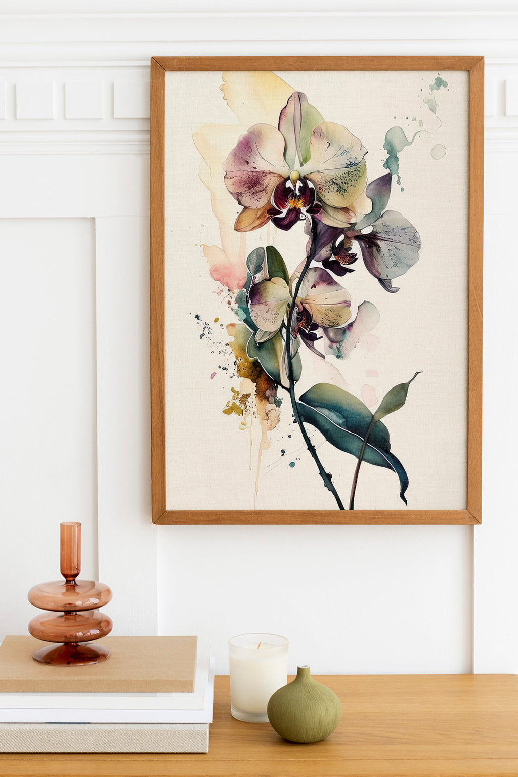 a framed painting of a vibrant orchid flower hanging on a wall above a wooden table. The table also holds a stack of books, a small green vase, and a white candle.