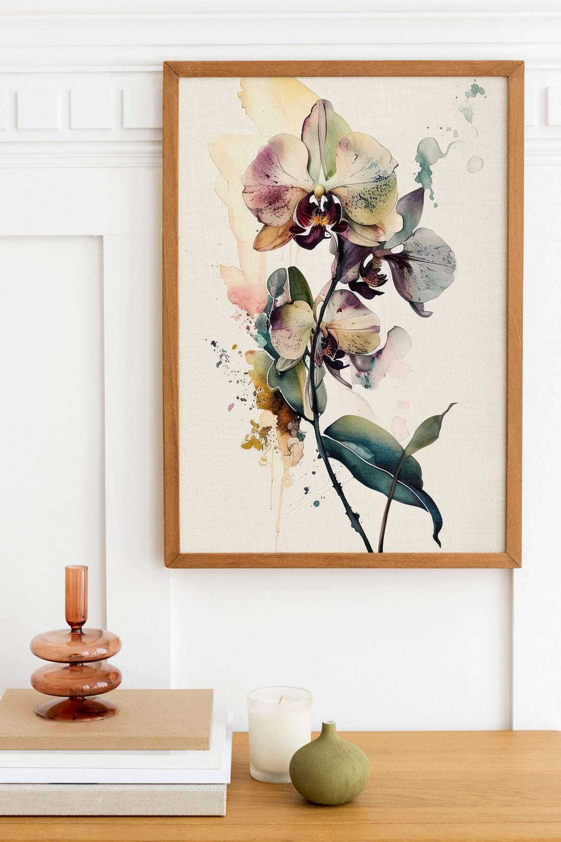 a framed painting of a vibrant orchid flower hanging on a wall above a wooden table. The table also holds a stack of books, a small green vase, and a white candle.