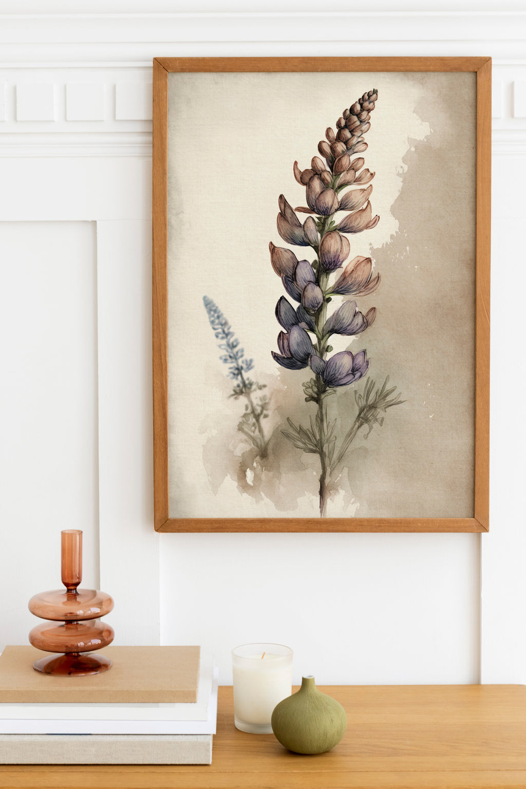 a framed watercolor painting of a purple flower on a white wall, with a wooden shelf below it holding a stack of books, a small green vase, and a white candle.