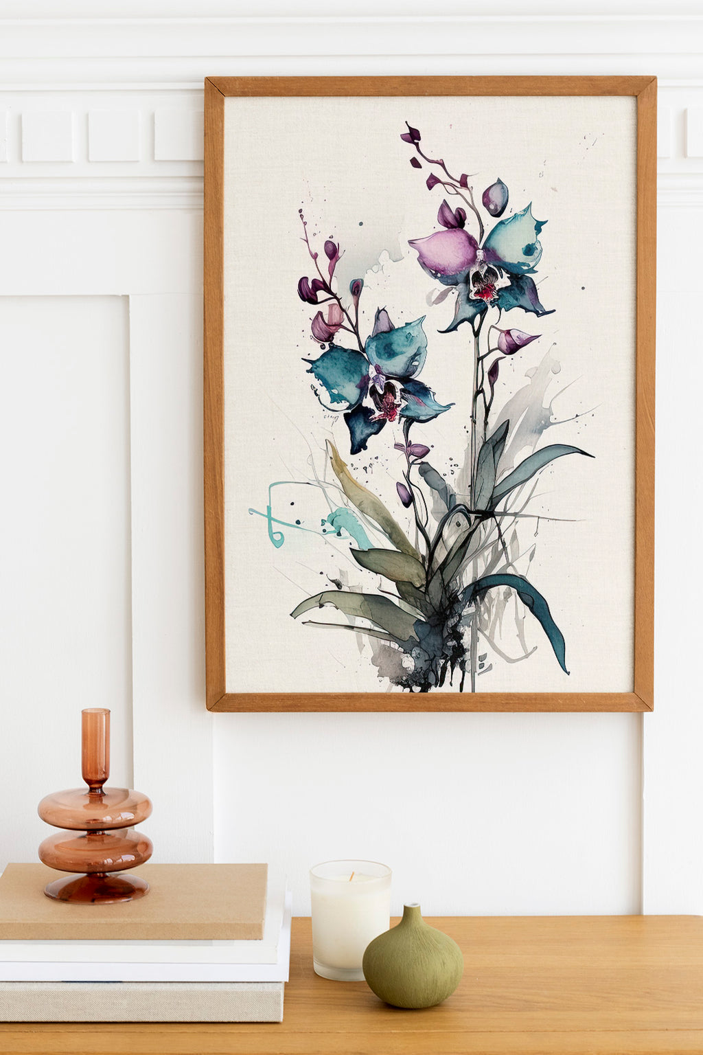 a framed painting of purple orchids hanging on a wall above a wooden table with various decorative items, including a candle, a stack of books, and a small green vase.