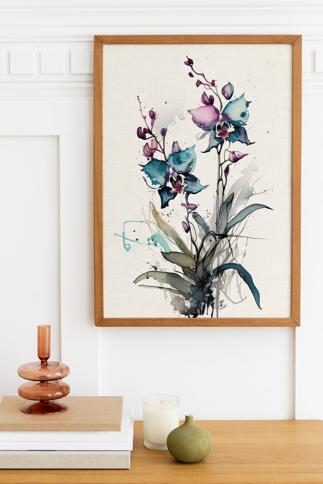 a framed painting of purple orchids hanging on a wall above a wooden table with various decorative items, including a candle, a stack of books, and a small green vase.