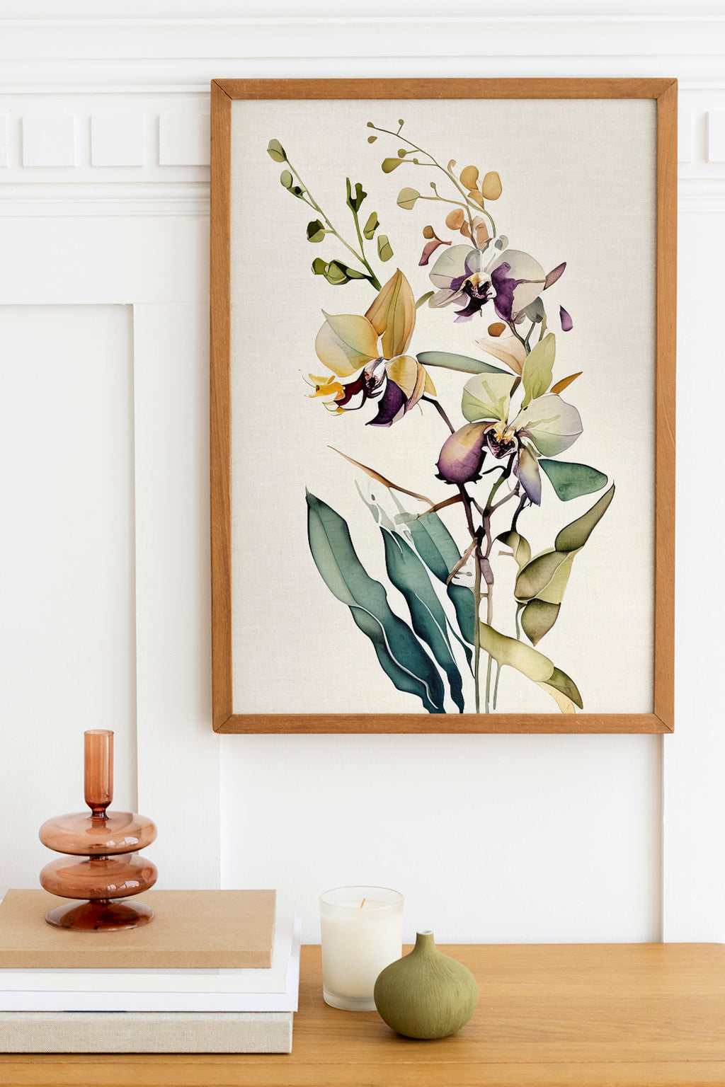 a framed painting of a floral arrangement hanging on a wall above a wooden table with various decorative items, including a candle, a small green vase, and a stack of books.