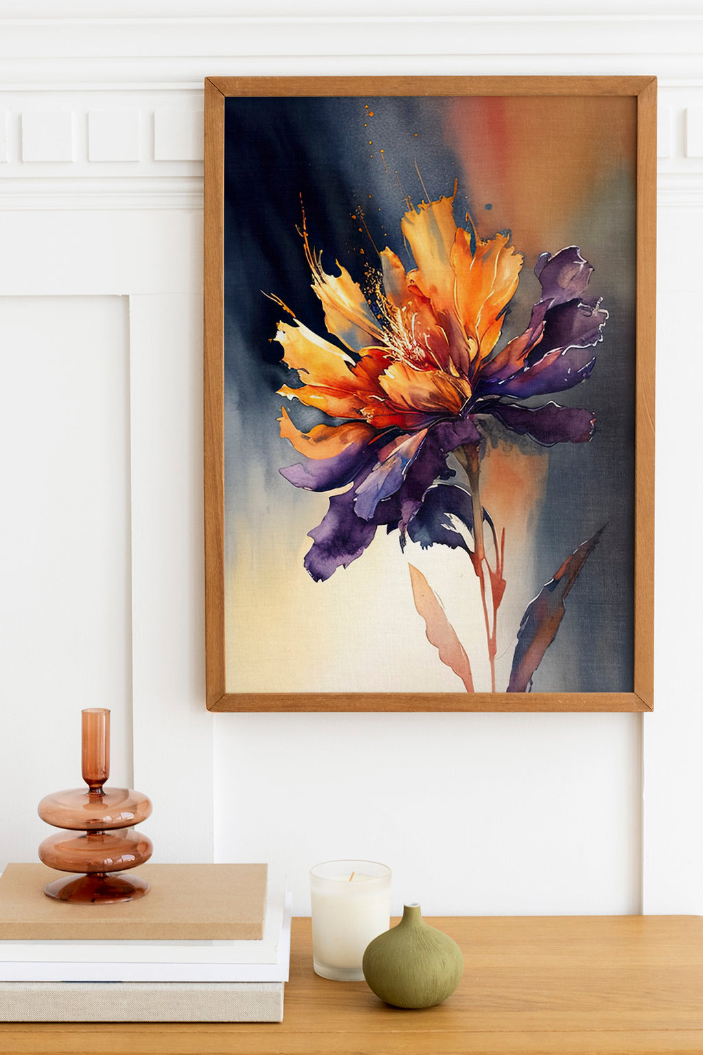 a framed painting of a vibrant, colorful flower hanging on a wall above a wooden table. The table has a stack of books, a small green vase, and a white candle.