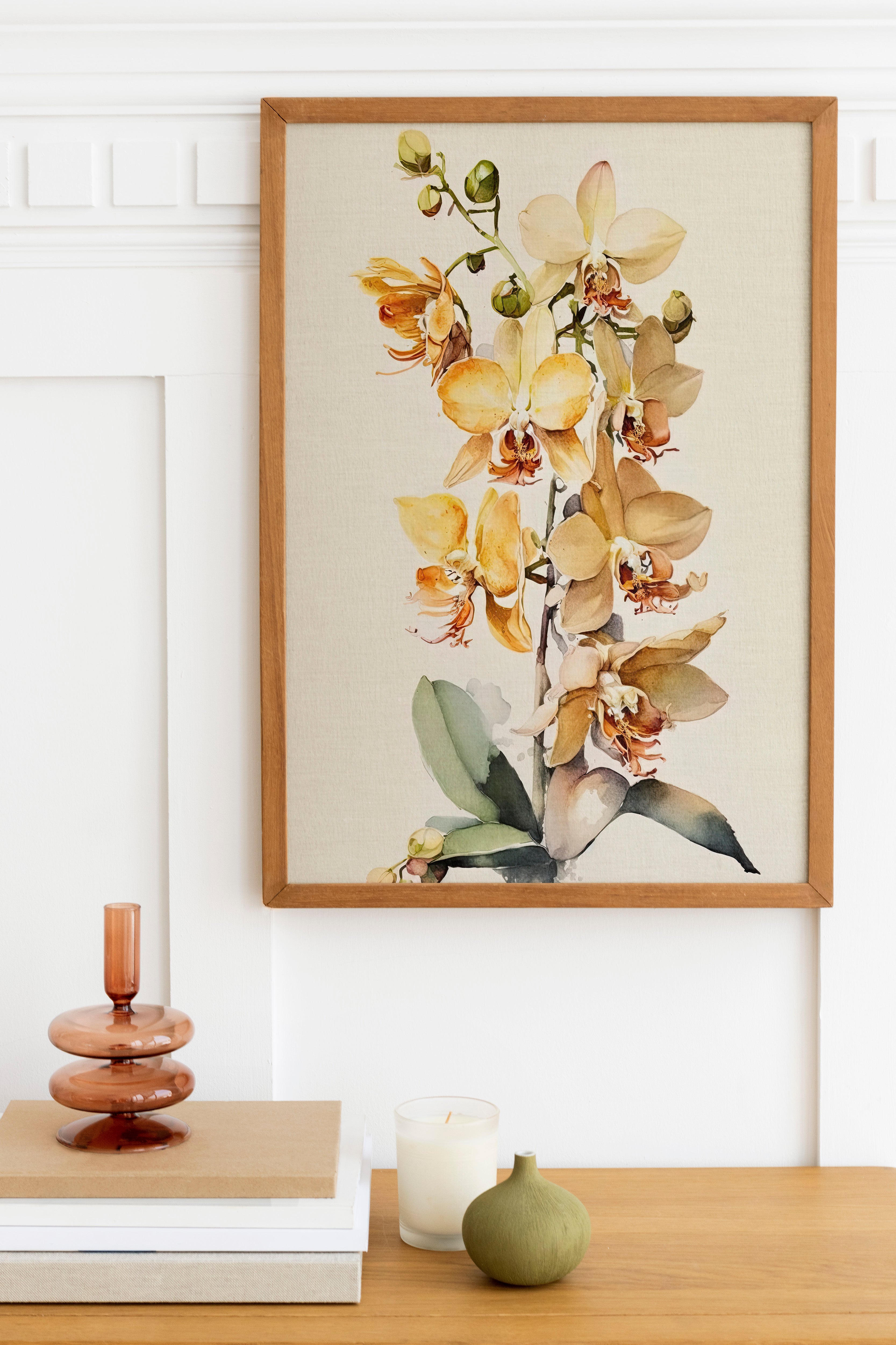 a wooden table with a framed painting of a yellow orchid plant hanging above it. The table also has a stack of books, a small green vase, and a white candle.