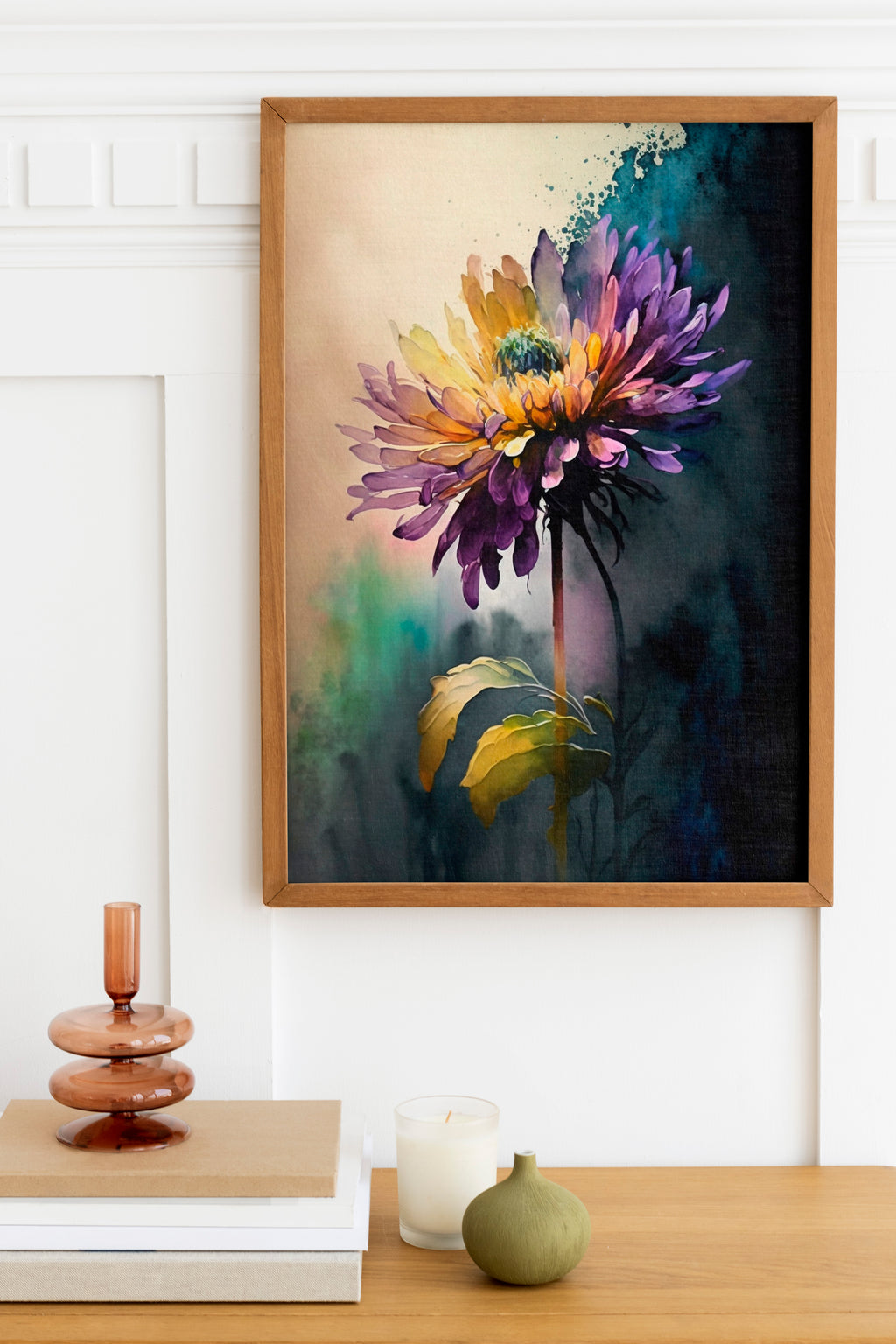 a framed painting of a vibrant purple and yellow flower hanging on a wall above a wooden table. The table has a stack of books, a small green vase, and a white candle.