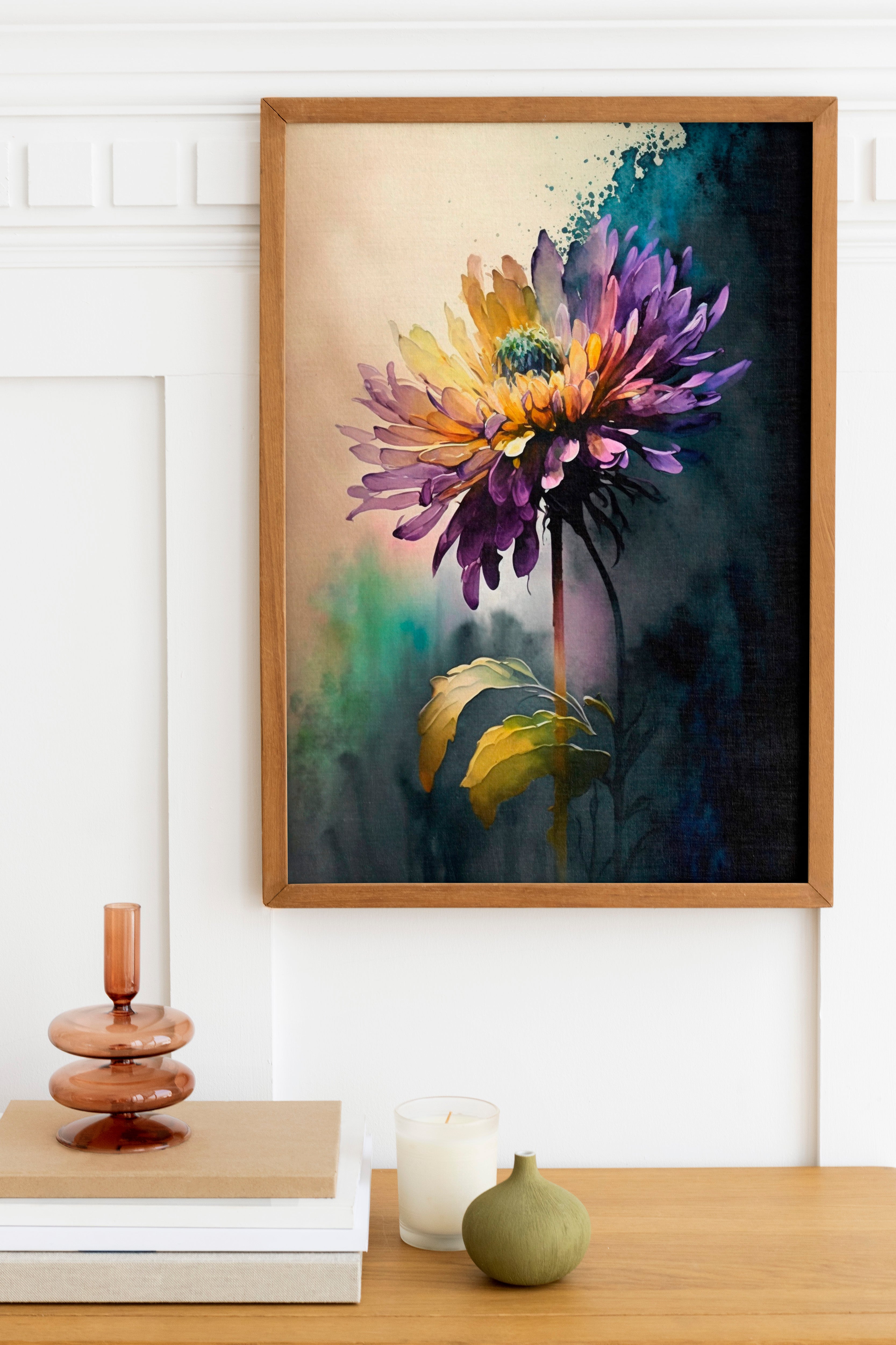 a framed painting of a vibrant purple and yellow flower hanging on a wall above a wooden table. The table has a stack of books, a small green vase, and a white candle.