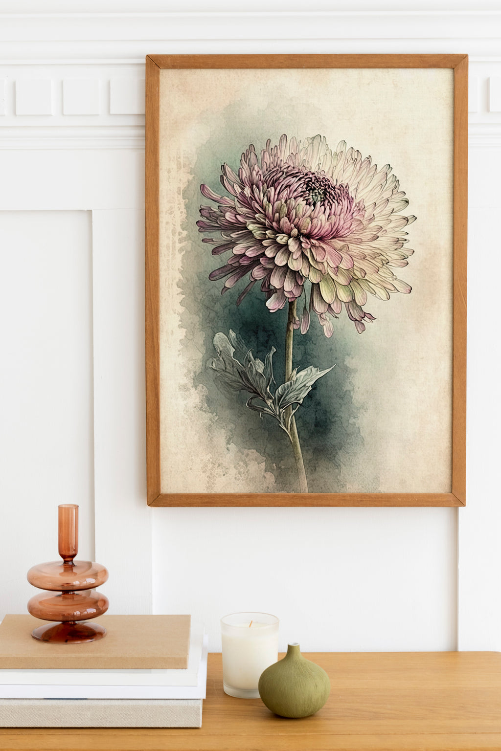 a framed painting of a large, vibrant purple chrysanthemum flower hanging on a white wall above a wooden table. The table also holds a small green vase, a white candle, and a stack of books.