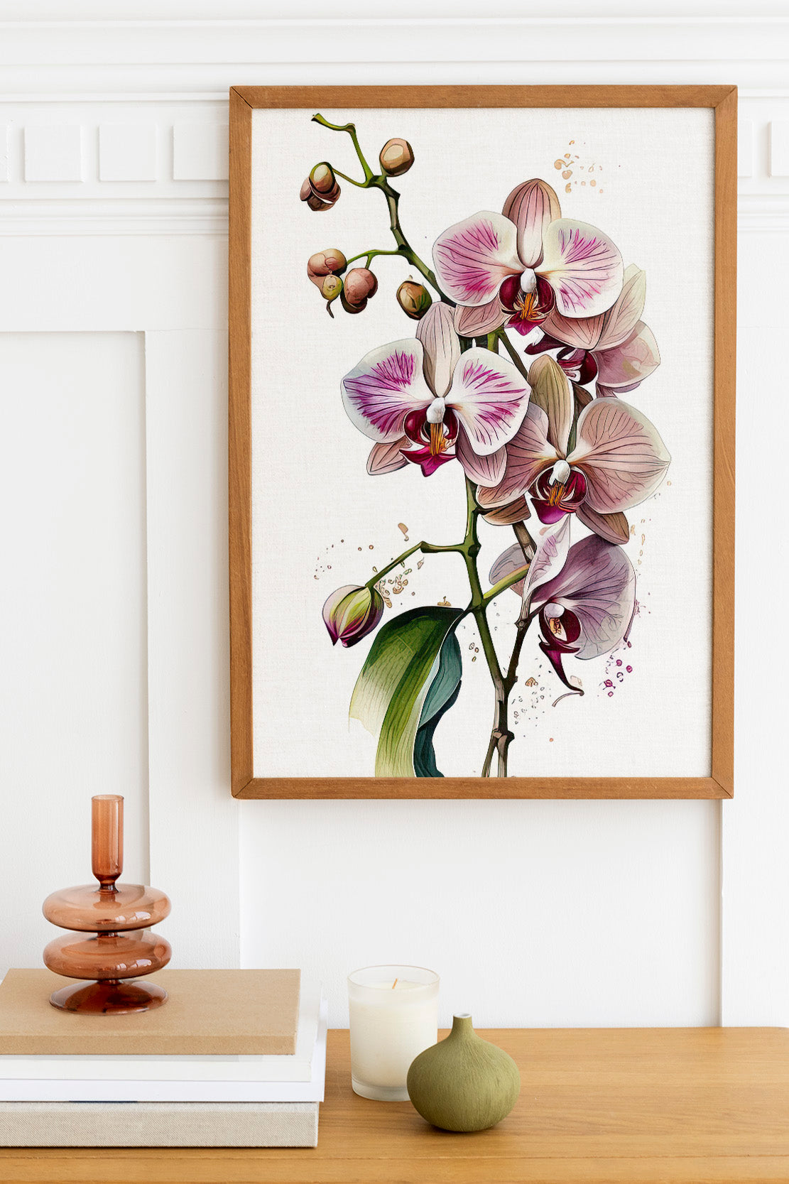 a framed painting of a purple orchid plant hanging on a white wall above a wooden table. The table has a stack of books, a small green vase, and a white candle.